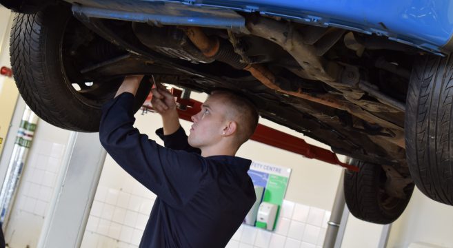 Male student pictured working underneath a car