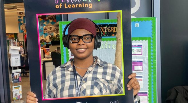 Student holding Festival of Learning Sign and smiling